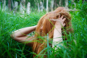 beautiful young sexy redhead woman with long red curly hair outdoor in high green grass and playing with her hair on face