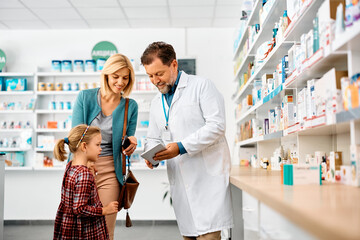 Wall Mural - Happy mother and daughter using touchpad with their pharmacist in pharmacy.