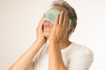 Older man with a warn compress over his eyes for pain relief