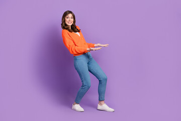 Sticker - Full length photo of impressed funny woman dressed orange cardigan carrying arms empty space isolated purple color background