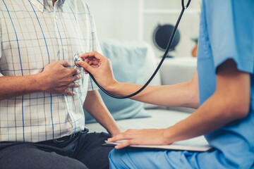 Caring young female doctor examining her contented senior patient with stethoscope in living room. Medical service for elderly, elderly sickness, declining health.