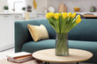 Spring interior. Bouquet of beautiful yellow tulips and books on wooden table in living room, space for text