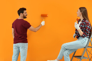 Poster - Man painting orange wall and woman sitting on folding ladder. Interior design