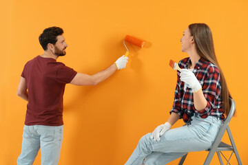 Wall Mural - Man painting orange wall and woman with brush. Interior design