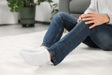 Poster - Man suffering from leg pain on white carpet at home, closeup