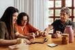 © kleberpicui - Adult granddaughter and grandparents having fun at the dinner table playing dominoes