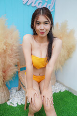 Wall Mural - Sexy Asian woman wearing yellow bikini sit on a chair Beside the swimming pool at Pool Villa