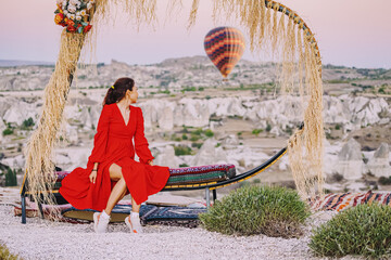 Wall Mural - Girl sitting on a decorated heart-shaped bench on a viewpoint and admiring view of Cappadocia hot air balloons