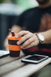 © Cavan Images - Close-up picture of guy drinking coffee to go on wooden table