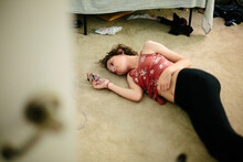 Teen Girl Lays On The Carpeted Floor Of Her Room Looking At Her Phone