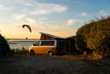 Paraglider In Golden Sunset Near Her Mini Van And Looking On The Ocean At Summer In Camping Natural Area