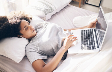 Canvas Print - Music earphones, woman and laptop in bed in bedroom for social media or internet browsing in the morning. Technology, relax or black female with computer for streaming podcast, audio or radio in home