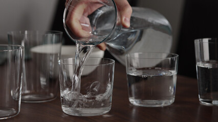 Man pour water into glasses from carafe on walnut table