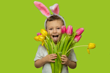 Happy Easter. A Child In A Rabbit Costume Holds A Bouquet Of Yellow And Pink Tulips. A Charming Baby With Funny Bunny Ears. Spring Easter Holiday. The Concept Of A Happy Childhood.