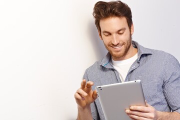 Sticker - Happy white man working using tablet computer leaning against white wall. Copy space, casual clothing.