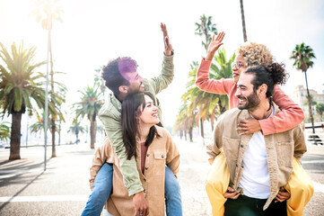 Group of young people piggy backs having fun together in the city street - Couples of students giving high-five - Multicultural friends walking outside university campus - Youth culture and travel