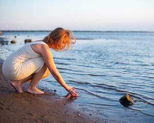 girl on the sandy seashore touches the water with her hands