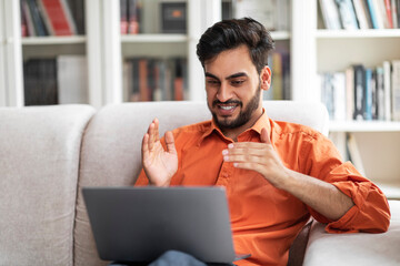 Wall Mural - Cheerful arab guy have video call with friends, home interior