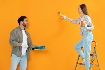 Sticker - Woman painting orange wall and man holding container with roller. Interior design