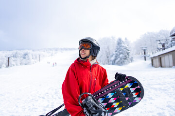 Portrait of Young Asian woman holding snowboard standing on snowy mountain at in ski resort. Attractive girl enjoy outdoor lifestyle extreme sport freeride snowboarding on winter holiday vacation