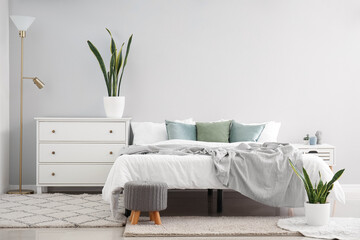 Interior of light bedroom with drawers, lamp and houseplants