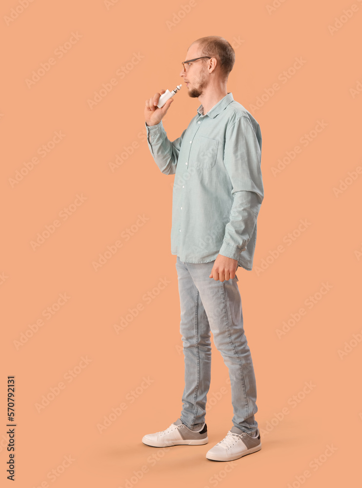 Young man in eyeglasses with disposable electronic cigarette on beige background