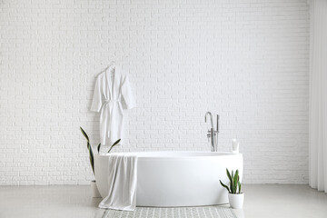 Interior of light bathroom with bathtub and houseplants