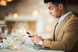 © Allistair F/peopleimages.com - Man, texting and phone at restaurant table for food, night and waiting for valentines day date. Young male, smartphone and wine glass for fine dining, bottle service or drink at dinner celebration