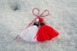 Closeup of a red and white martenitsa (martisol) with wooden beads sitting on the snow. Martenitsa is a symbol of the approaching spring - tradition in Bulgaria, Romania and Moldova.