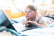 © Cavan Images - Tween working on laptop looking bored at home on sunny day
