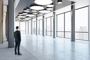 Sticker - Man in black suit looking on city skyscrapers on background from business center high floor stylish hall with metallic pillars and panoramic window