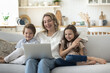 © fizkes - Happy mom and cheerful kids relaxing on sofa at cozy home together, watching movie, enjoying cartoon, leisure, talking on video call, using laptop for Internet communication, laughing