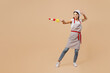 Full body young housewife housekeeper chef baker latin woman wear striped apron toque hat making grilled vegetables on metal skewer pov fencing isolated on plain beige background. Cook food concept.