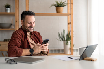 Handsome businessman holding smartphone using mobile technology checking corporate apps, smiling, looking satisfied. Professional manager in home office typing on cellphone, checking new e-mails.