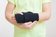 Little child hand with protective black elastic wrist bandage isolated on light gray wall background. Closeup. Front view.