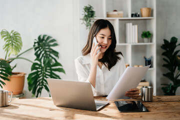 Business asian woman Talking on the phone and using a laptop with a smile while sitting at home office