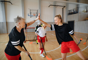 Sticker - Group of young and old cheerful women, floorball team players, in gym cebrating victory.