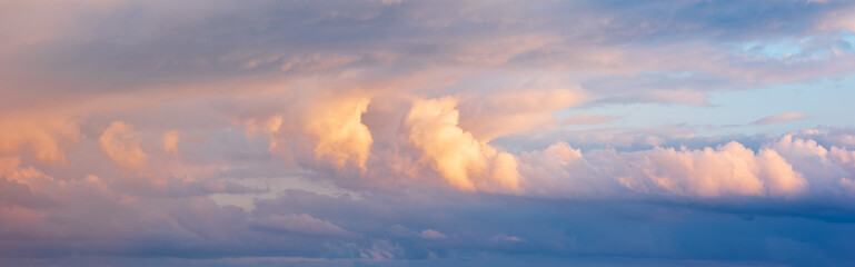 Wall Mural - Panoramic background of evening sky with strom clouds glowing in the light of the setting sun