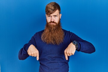 Canvas Print - Redhead man with long beard wearing casual blue sweater over blue background pointing down looking sad and upset, indicating direction with fingers, unhappy and depressed.