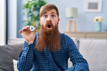 Canvas Print - Caucasian man with long beard holding virtual currency bitcoin scared and amazed with open mouth for surprise, disbelief face