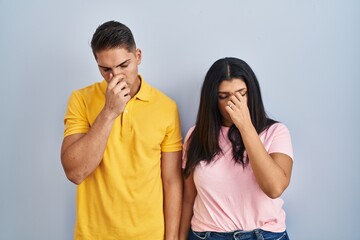 Canvas Print - Young couple standing over isolated background tired rubbing nose and eyes feeling fatigue and headache. stress and frustration concept.