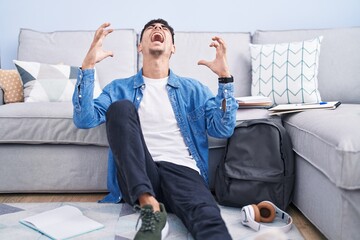 Sticker - Young hispanic man sitting on the floor studying for university celebrating mad and crazy for success with arms raised and closed eyes screaming excited. winner concept