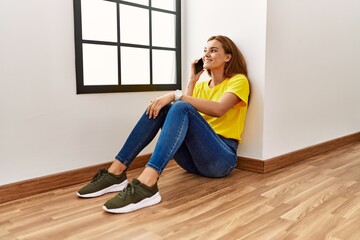 Wall Mural - Young woman talking on the smartphone sitting on floor at empty room