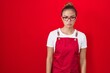 Young hispanic woman wearing waitress apron over red background skeptic and nervous, frowning upset because of problem. negative person.