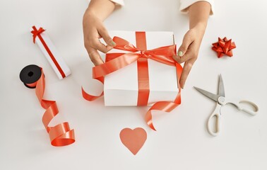 Young beautiful hispanic woman preparing christmas gift on table over isolated white background