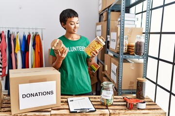 Sticker - Young hispanic woman wearing volunteer uniform holding food at charity center