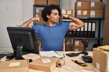 Poster - Hispanic man with curly hair working at small business ecommerce showing arms muscles smiling proud. fitness concept.