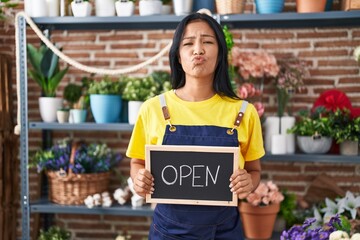 Poster - Hispanic woman working at florist holding open sign looking at the camera blowing a kiss being lovely and sexy. love expression.