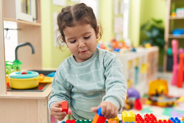 Wall Mural - Adorable hispanic toddler playing with construction blocks standing at kindergarten