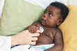 African american baby having medical examination sitting on bed at bedroom